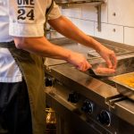 man touching meat patty on turner on grill